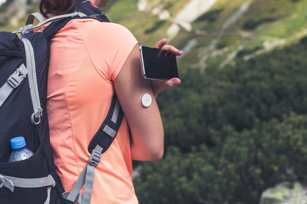Active life of diabetics, woman hiking and checking glucose level with a remote sensor and mobile phone