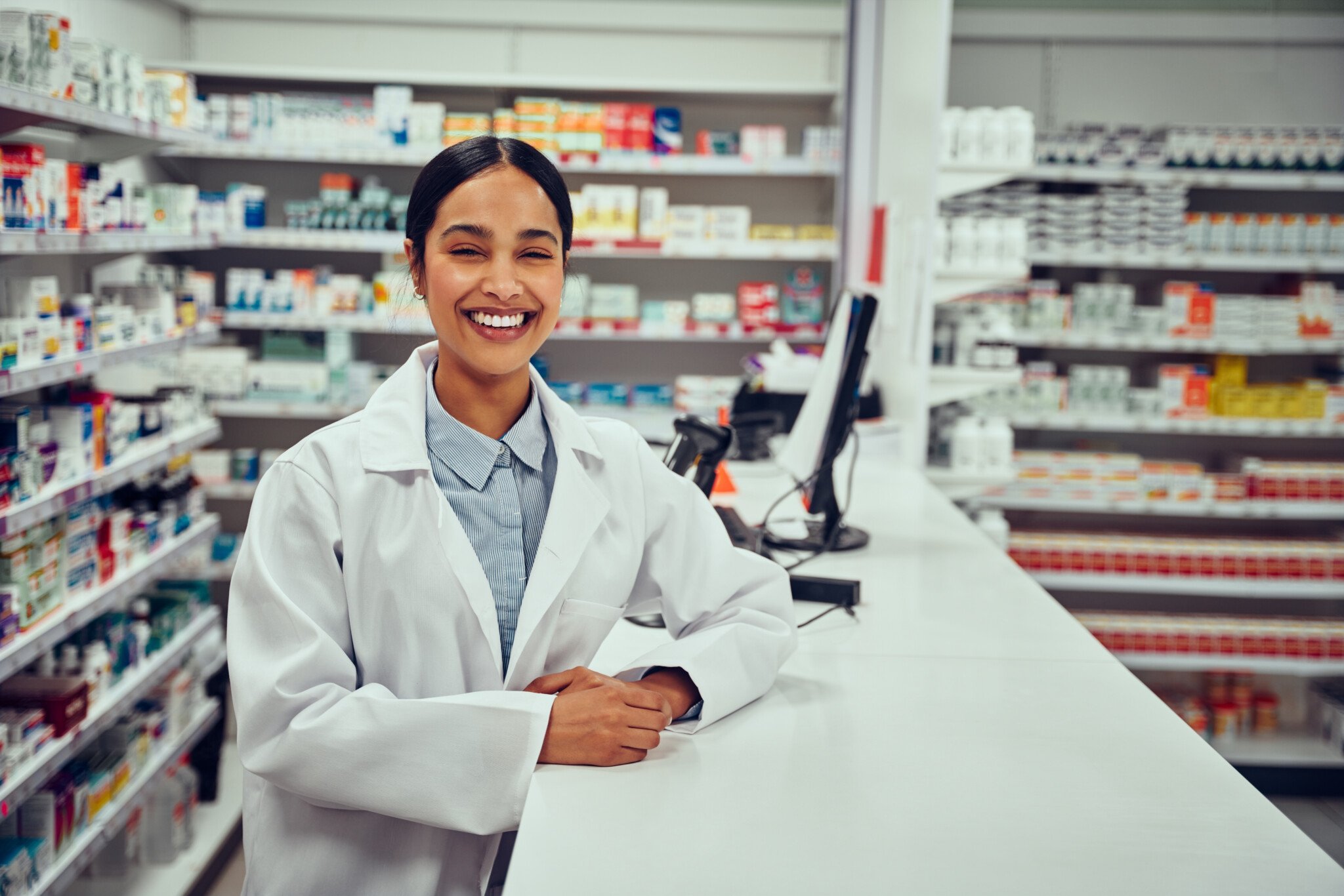 Smiling happy young woman pharmacist leaning on a desk in the pharmacy